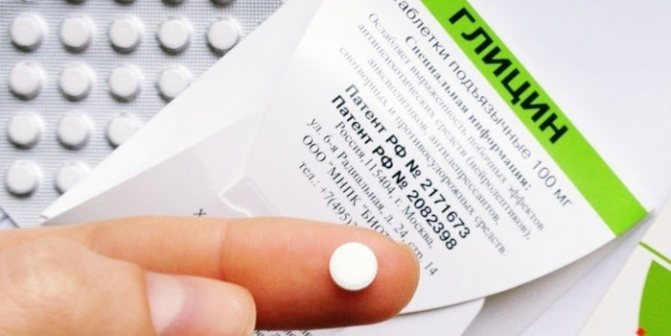 Таблетка глицина на пальце на фоне упаковки таблеток
